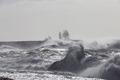 Waves splashing on shore against clear sky