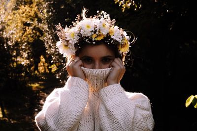 Portrait of woman wearing flowers on head against trees