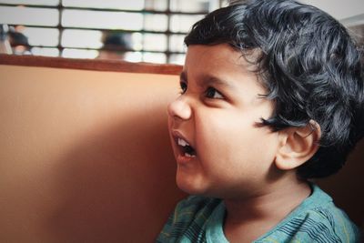 Close-up of boy looking away while making face by wall