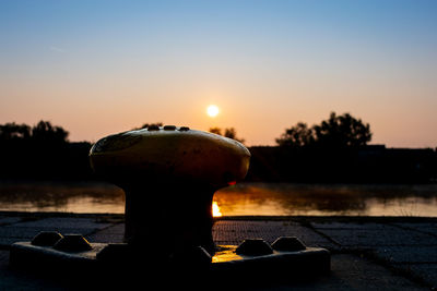 Close-up of orange metal by lake against sky during sunset