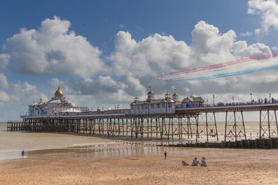 View of beach against cloudy sky with the red arrows flying over eastbourne pier