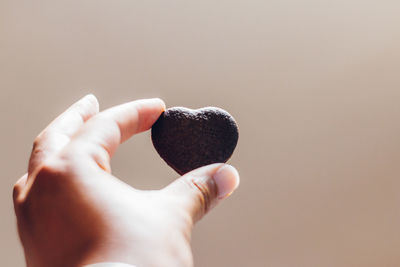 Close-up of man holding heart shape brown cookie against white background