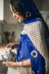 Young woman holding teapot while standing in kitchen at home