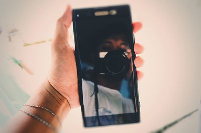 Reflection of man holding camera on mobile screen