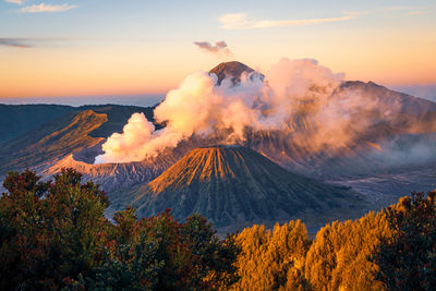 Smoke emitting from volcanic mountain against sky during sunset