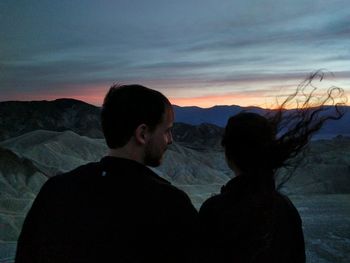 Silhouette friends on mountain against sky during sunset