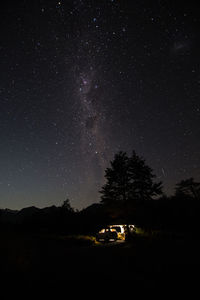 Car on illuminated road amidst trees against sky at night