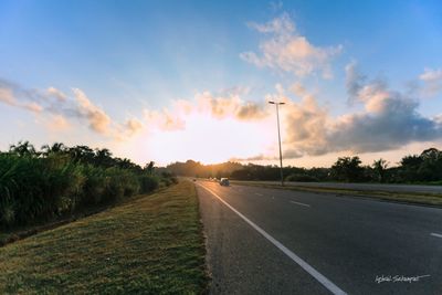 Road amidst field against sky during sunset