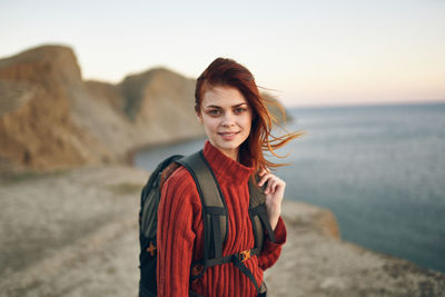 Portrait of smiling young woman standing on beach during sunset