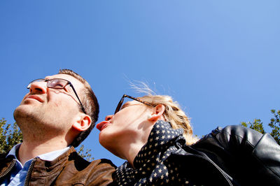 Low angle view of woman sticking out tongue while sitting by boyfriend against clear blue sky