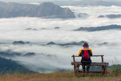 Rear view of man sitting on mountain against sky