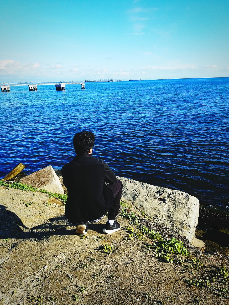 REAR VIEW OF A MAN SITTING ON SEA SHORE