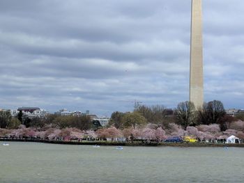 View of city at waterfront against cloudy sky