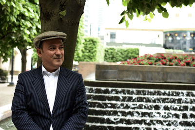 Mid adult man looking away while standing against tree