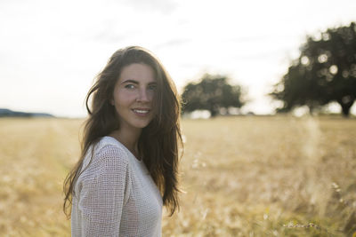 Portrait of smiling young woman standing on field against sky