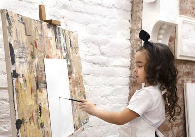 Dreamy pretty kid girl with paintbrush near drawing easel. little painting artist.