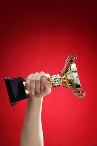 Cropped hand of woman holding trophy against red background