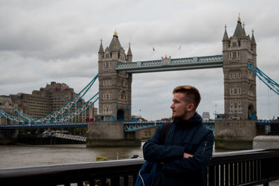 Man with arms crossed standing against tower bridge