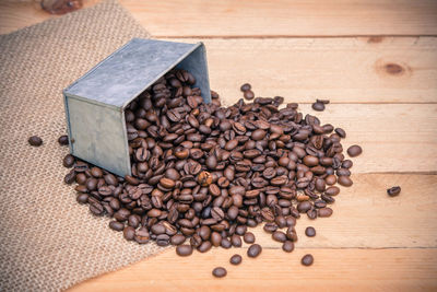 Roasted coffee beans spilling from metallic container on table