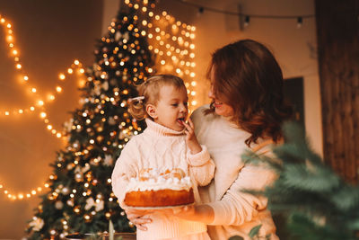 Mom and daughter in sweaters together prepare festive cake for the christmas holiday in the kitchen