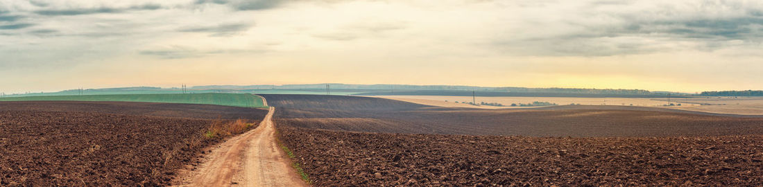 Field road between plowed fields in autumn under gray sky. soil preparation for sowing. panoramic