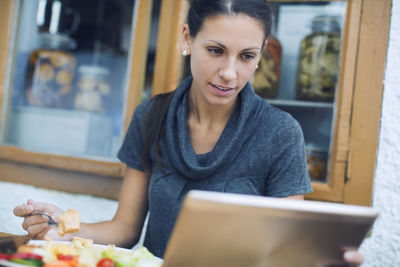 Woman using digital tablet while having lunch in cafe