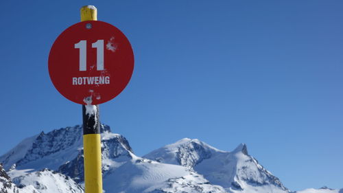 Road sign by snowcapped mountains against clear blue sky