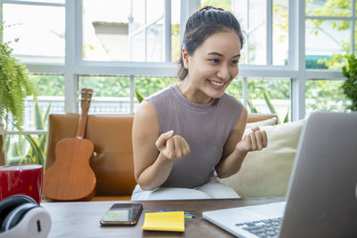 Smiling woman celebrating while looking at laptop in greenhouse