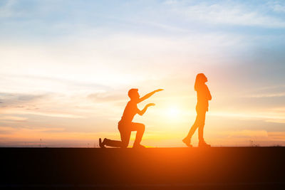 Silhouette man and woman against sky during sunset