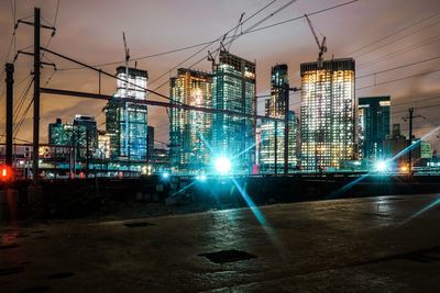 Illuminated street amidst buildings against sky at night