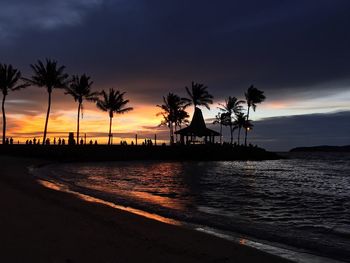 Silhouette palm trees on beach against sky at sunset