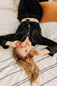 A happy pretty young woman in pajamas is resting and having breakfast in bed in a cozy apartment