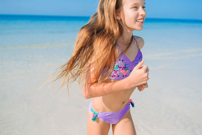 Smiling girl wearing bikini running in beach