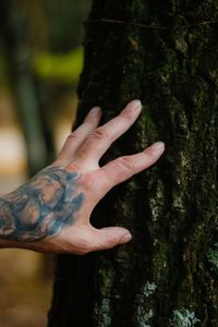 Cropped image of man with tattooed hand touching tree trunk at park