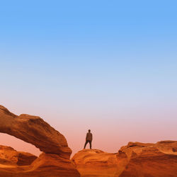 Rear view of man standing on rock formation against blue sky