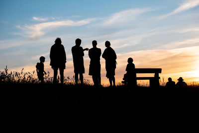 Silhouette people standing on land against sky during sunset