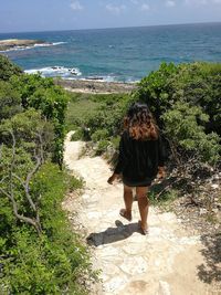 Rear view of woman walking on footpath against sea