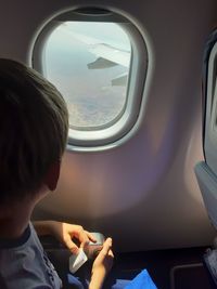 Boy looking through window while traveling in airplane