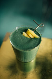 Green spirulina smoothie with pineapple on brass, gold table and teal background