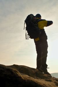 Tourist with backpack and poles in hands stand on cliff and watching into deep misty valley bellow.