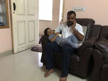 Father answering mobile phone while son lying on his laps at home