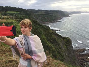 Woman taking selfie while standing on cliff against sea