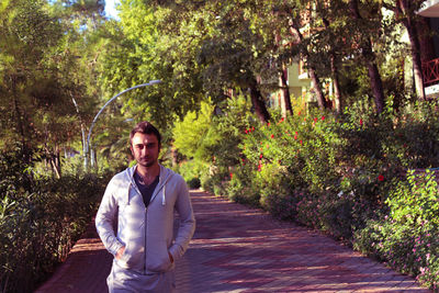 Portrait of young man standing on footpath amidst plants