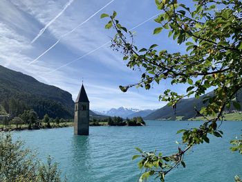 Churchtower on lago di resia - italy. scenic view of lake by mountains against sky