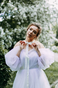 A elegant young woman bride in a wedding dress walks alone in a blooming spring outdoor park