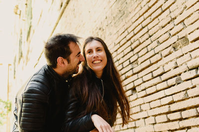Smiling couple standing by brick wall