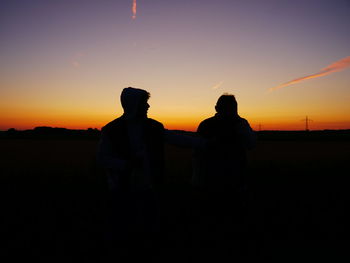 Silhouette couple standing against orange sky during sunset