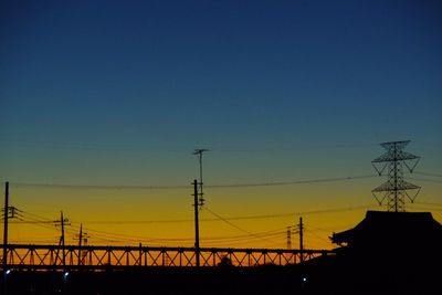 Silhouette electricity pylons against clear sky at sunset