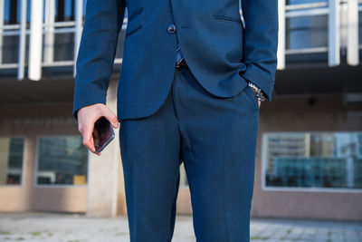 Midsection of businessman holding mobile phone while standing in city