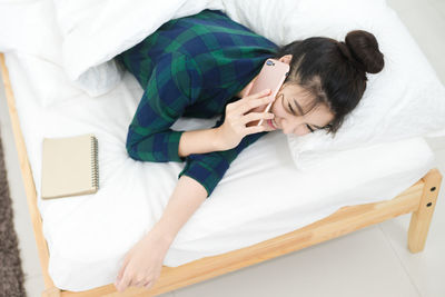 High angle view of woman answering smart phone while lying on bed at home